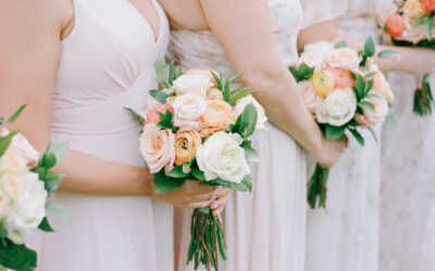 Bridesmaids hold colorful floral bouquets during an outdoor wedding ceremony in a soft, natural setting on a sunny day