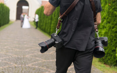 Professional wedding photographer takes pictures of the bride and groom in garden, the photographer in action with two cameras on a shoulder straps.