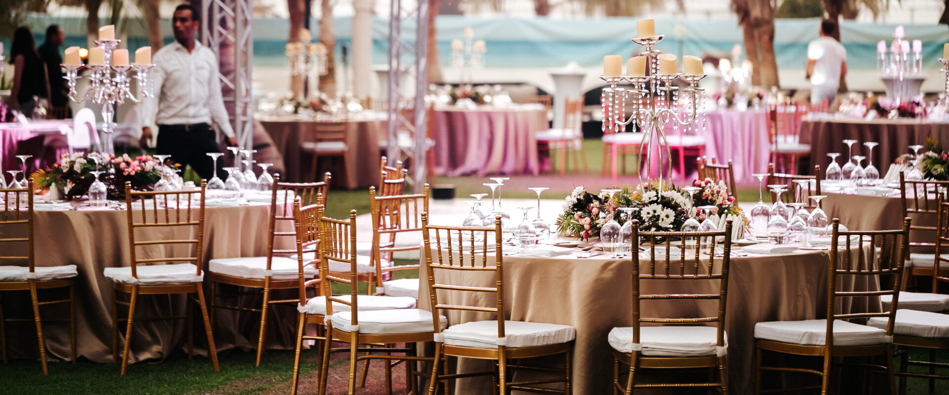 International Wedding outdoor celebration EVENING party under palm trees. Served tables on green area in hotel. Landyard. Beige and pink colors. Close-up and wide angle.